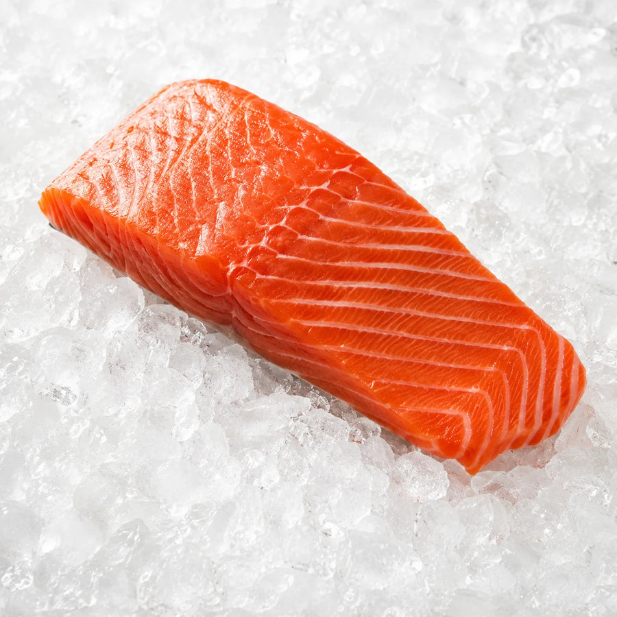 A thick slice of fresh salmon fillet with bright orange-pink flesh and white marbling, resting on crushed ice.