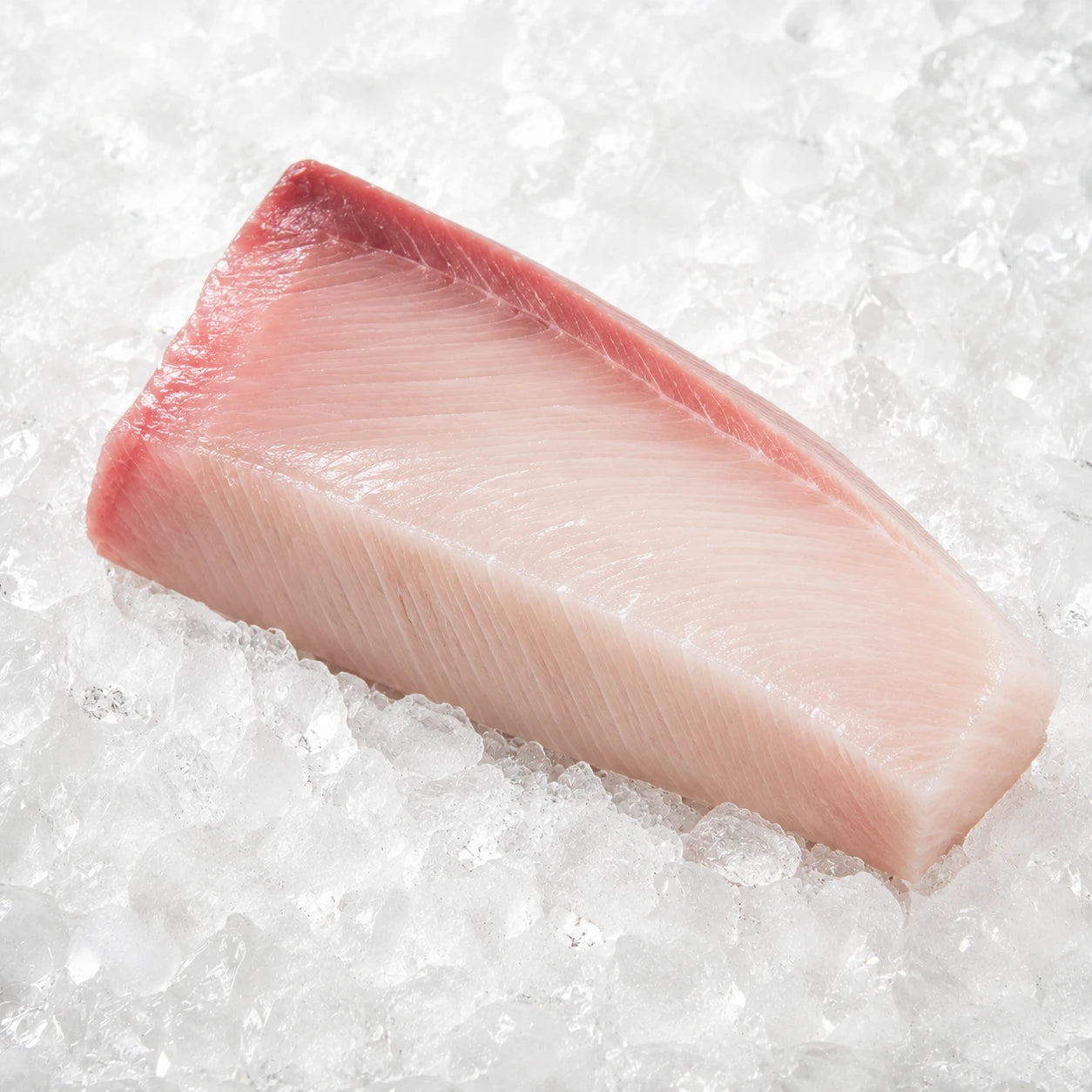 A raw fish fillet with a pink-red skin and pale pink-white meat, resting on a bed of crushed ice.