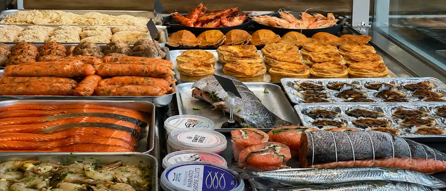 A large buffet-style food display filled with assorted cooked and raw seafood, including shrimp, fish, prawns, mussels, and various prepared dishes in metal trays.